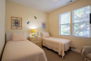 A bedroom with two beds, a nightstand, a lamp, and artwork on the walls. - Mellow Yellow (Carolina Beach)