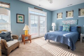 A bedroom with a bed, two nightstands, a lamp, a chair, and a window with blinds.