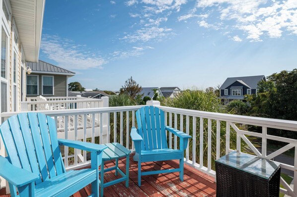 A wooden deck with two chairs and a table, overlooking a residential area with houses and greenery.