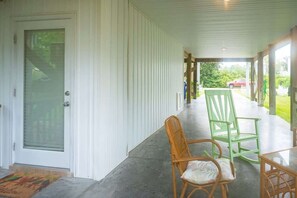 A covered porch with two wicker chairs, a table, and a glass door. - Mellow Yellow (Carolina Beach)