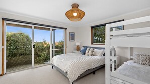A bedroom with a large sliding glass door leading to a garden, a bunk bed, and a hanging light fixture. - Pier Vista (Lorne)