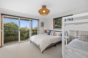 A bedroom with a large sliding glass door leading to a garden, a bunk bed, and a hanging light fixture. - Pier Vista (Lorne)