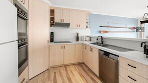 A modern kitchen with wooden cabinets, a built-in oven, a dishwasher, and a countertop with a sink. - Pier Vista (Lorne)