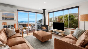 A modern living room with a large TV, leather sofas, a fireplace, and a view of the ocean. - Pier Vista (Lorne)