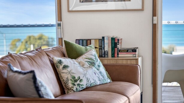 A living room with a leather sofa, a framed picture on the wall, and a bookshelf with books. - Pier Vista (Lorne)