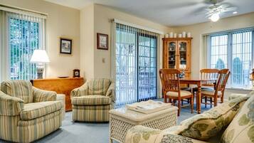 A living room with striped armchairs, a sofa, a dining table with chairs, a cabinet, and a ceiling fan.