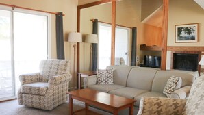 Una sala de estar con sofá, sillón y mesa de centro. Hay una chimenea y un televisor.