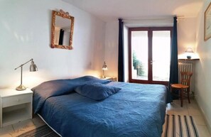 A bedroom with a bed, a nightstand, a lamp, a chair, and a window with curtains.