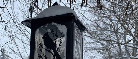 Ein Vogelhaus mit einer Vogelkontur an einem Zweig, umgeben von schneebedeckten Bäumen und Büschen.