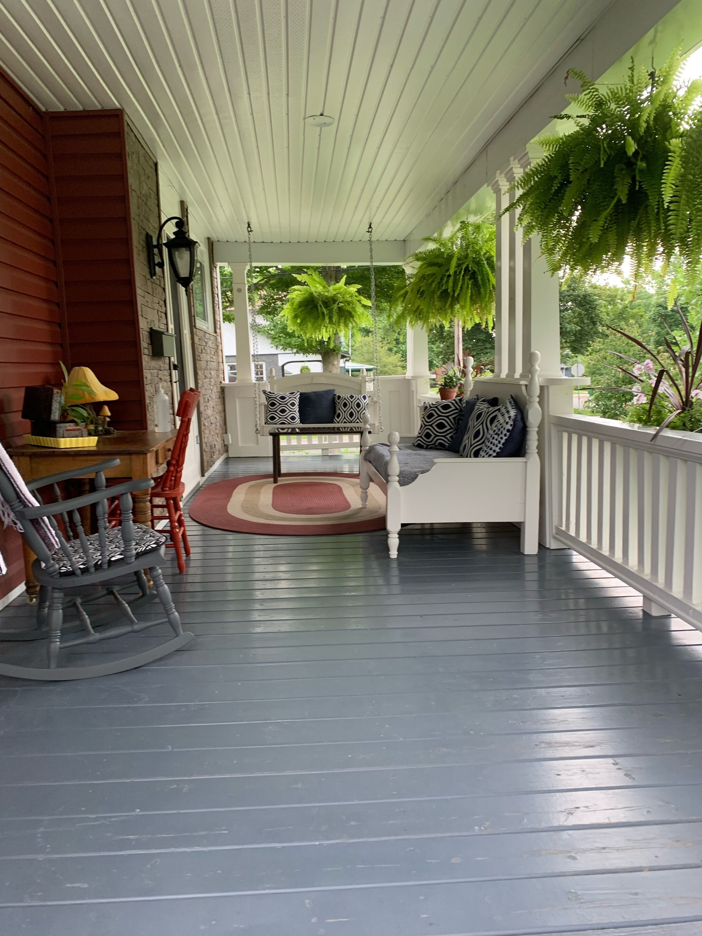 A porch with a rocking chair, a bench with patterned cushions, and a small table with a lamp.