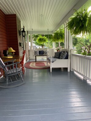 A porch with a rocking chair, a bench with patterned cushions, and a small table with a lamp.