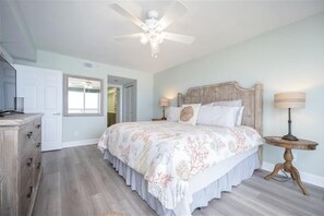 A bedroom with a wooden bed, two bedside lamps, a ceiling fan, and a dresser.