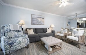 A living room with a grey sofa, floral armchairs, a wooden ottoman, and wicker chairs. - 7402 Towers 8 and 9 - 2/2 Oceanfront Beauty on Traffic Free Beach - Ponce Inlet (Ponce Inlet)