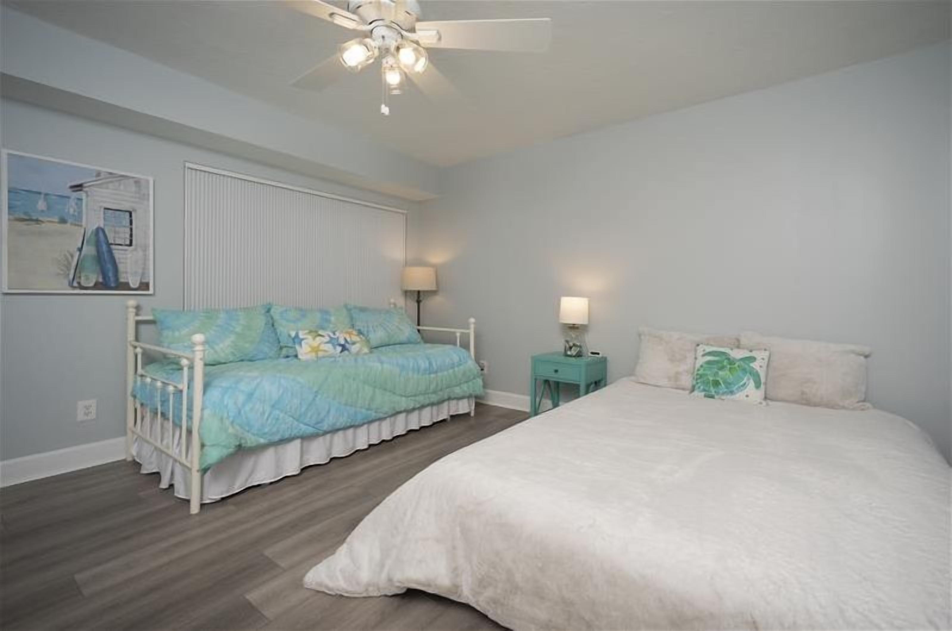 A bedroom with a bed, a nightstand, a ceiling fan, and a wall-mounted lamp.