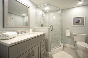 Un baño moderno con ducha de vidrio, un espejo grande y un inodoro.