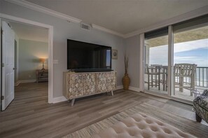 Amplia sala de estar con una televisión de pantalla plana, un mueble de madera y un gran ventanal corredero que da a un balcón con mobiliario exterior.