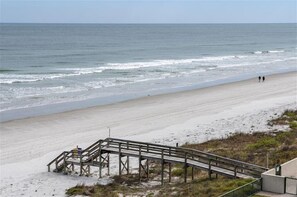 A beach with a wooden staircase leading down to the shore, a sandy beach, and the ocean in the background.