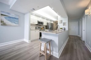 A modern kitchen with white cabinetry, a central island, and a wooden stool.