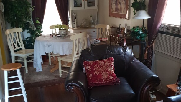 Una sala de estar con un sofá de cuero, una mesa de comedor, sillas y una alfombra estampada.