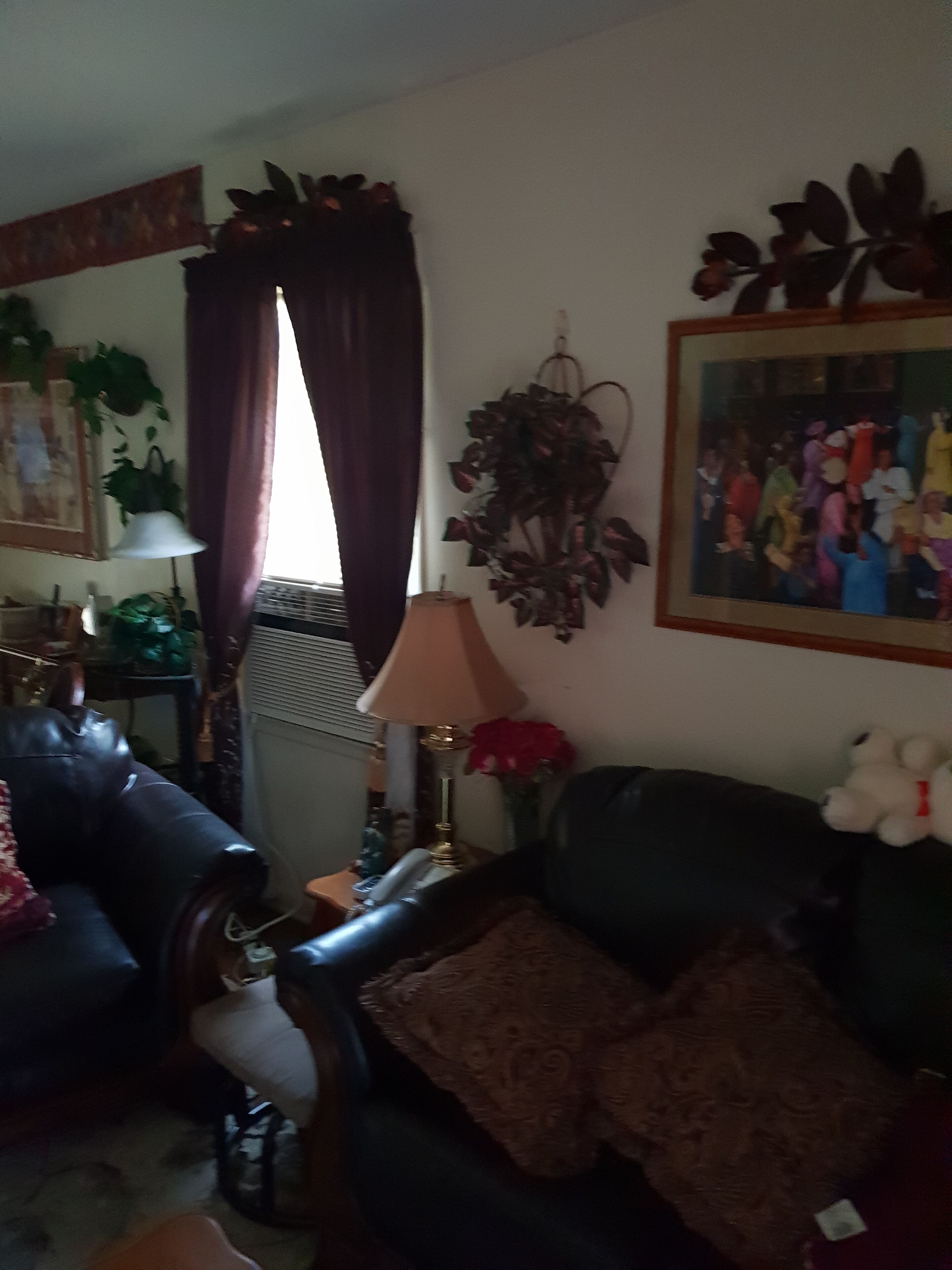 A living room with a dark leather sofa, a patterned throw pillow, a lamp, and a framed painting on the wall.