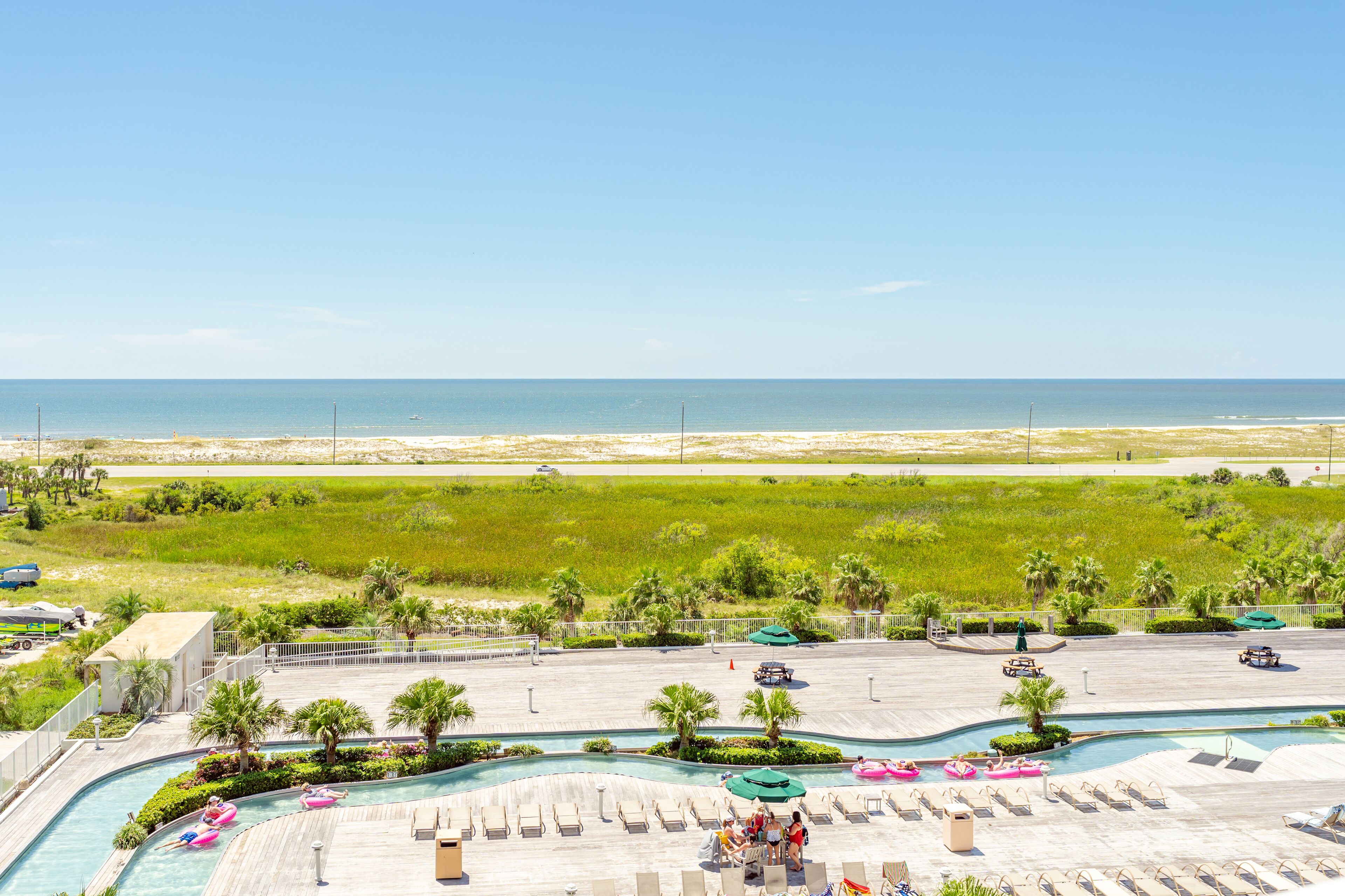 A resort pool area with a view of the beach, lounge chairs, and a swimming pool.