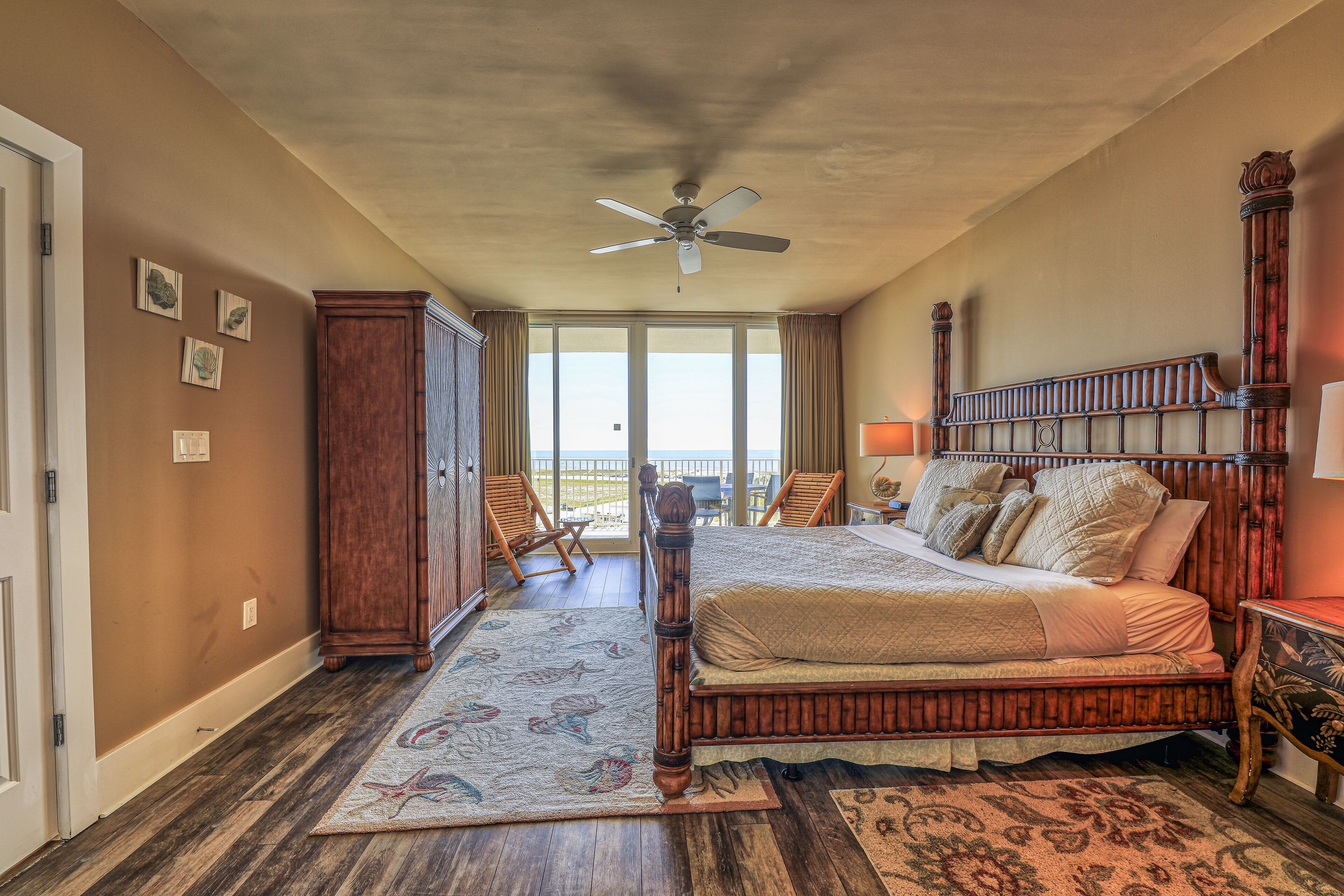 A bedroom with a large bed, a ceiling fan, and a view of the outdoors.