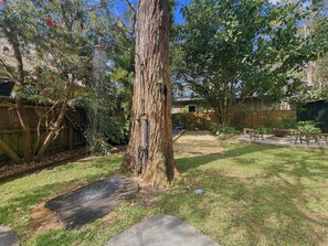 A backyard with a large tree, a wooden fence, and a concrete pathway. - Pearl Beach Semi - 2 min to sand & sea – Wattle (Pearl Beach)
