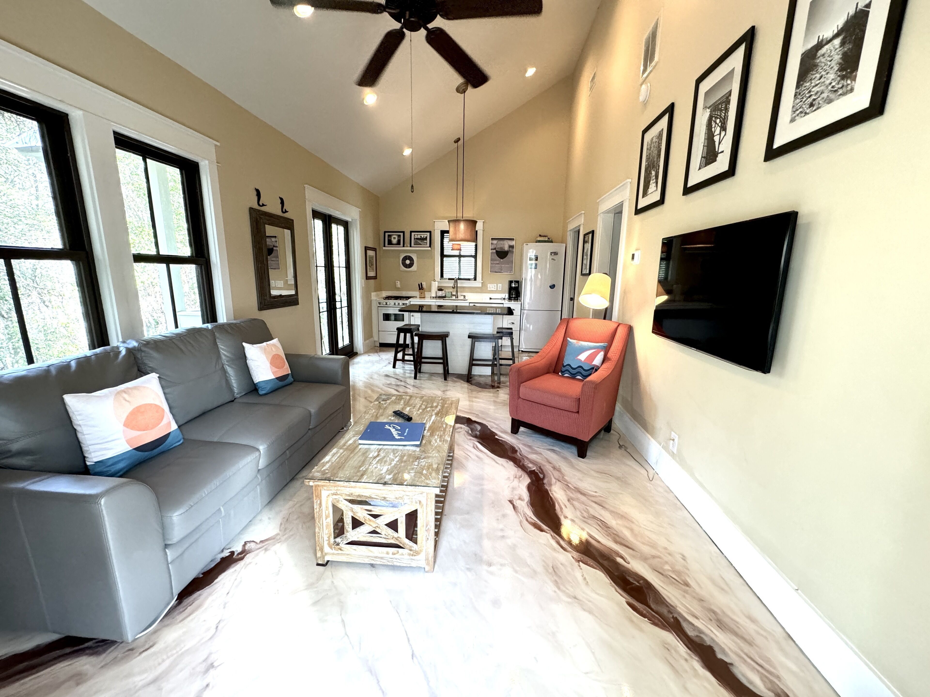 A living room with a gray sofa, a wooden coffee table, a red armchair, and a TV mounted on the wall.