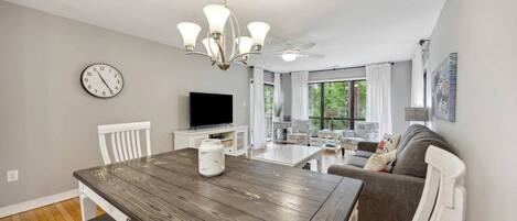 A modern living room with a dining area, a television, and a clock on the wall.