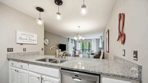 A kitchen with granite countertops, white cabinetry, a dishwasher, and a chandelier.
