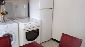 Une cuisine compacte équipée d’un lave-linge, d’un four et d’un réfrigérateur. On y trouve également une table à manger avec des chaises.