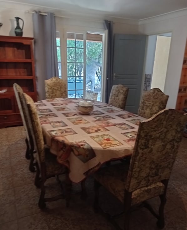 A dining room with a table covered in a patterned tablecloth, surrounded by four upholstered chairs.