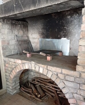 A stone-built fireplace with a metal grate and logs stored below.