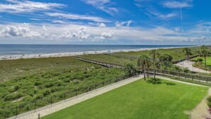 Un paysage côtier comprenant une plage, des zones herbeuses et une promenade pavée.