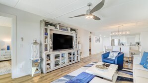 Un salon moderne doté d’un t éléviseur à écran plat, d’un ventilateur de plafond et d’un coin repas avec des meubles blancs.