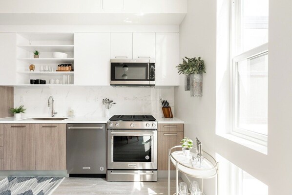 Una cocina moderna con armarios blancos, microondas integrado, estufa de acero inoxidable y lavavajillas.