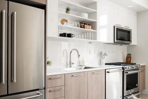 Une cuisine moderne dotée d’appareils électroménagers en acier inoxydable, de meubles blancs et d’un four à micro-ondes encastré.