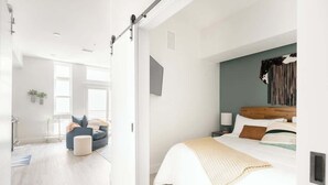 Een moderne slaapkamer met een bed, een zithoek met een stoel, en een groot raam.