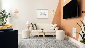 Un salon comprenant un canapé, une table basse, un téléviseur fixé au mur et un tableau encadré.