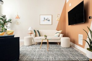 A living room with a sofa, a coffee table, a TV mounted on the wall, and a framed picture. - Colorful Western Vibe | Pet-Friendly | Zuni Lofts (Denver)