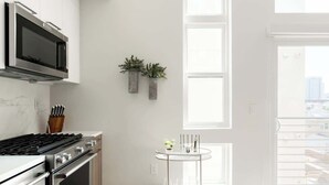Een moderne keuken met een ingebouwde magnetron, oven en gasfornuis. Twee potplanten hangen aan de muur en er staat een klein rond tafeltje met een vaas.