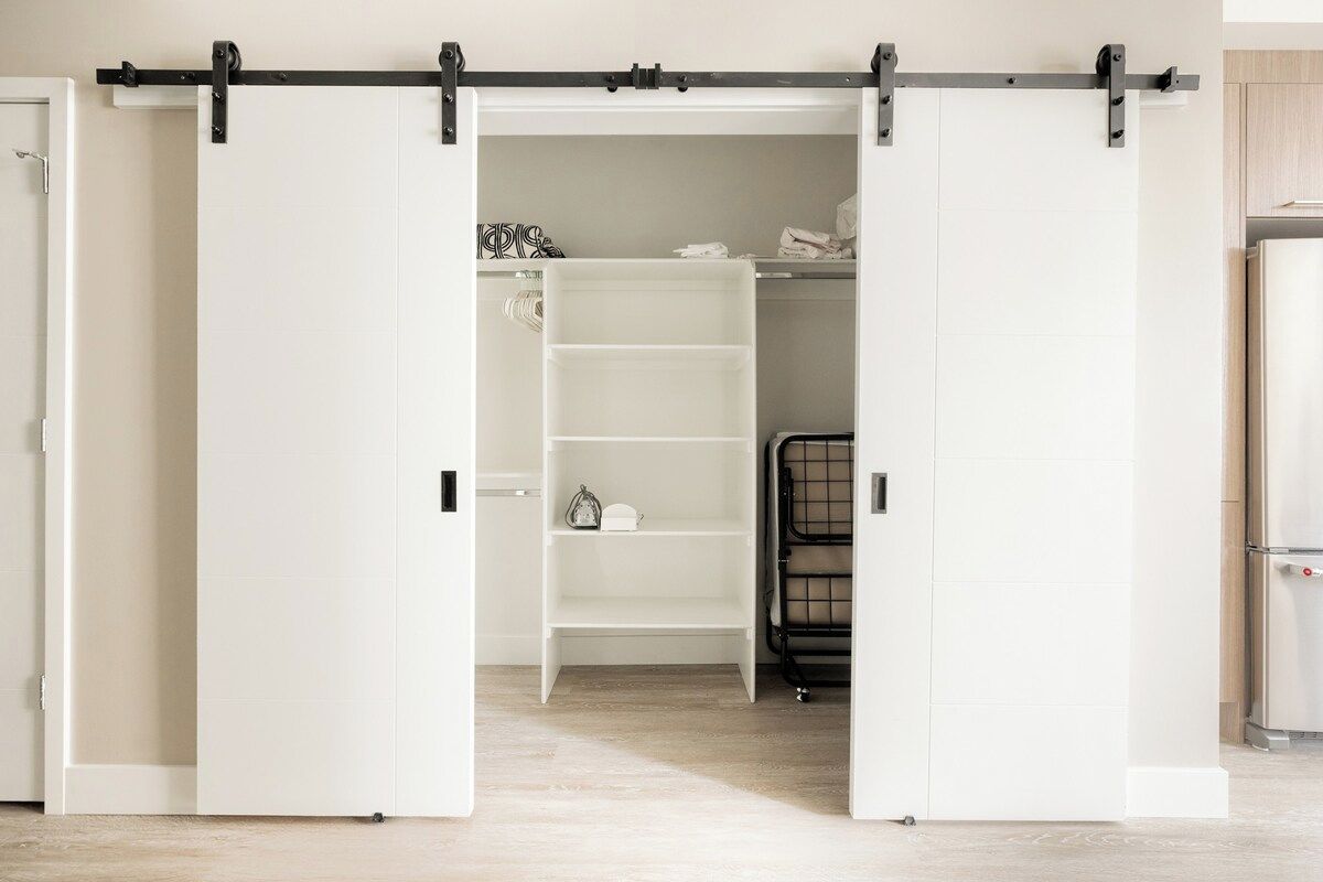 A room with a sliding closet door, a white shelving unit, and a black metal rack.