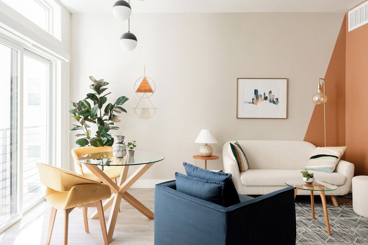 A modern living room with a sofa, a coffee table, and a dining area with chairs and a plant.
