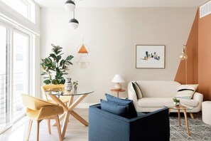 A modern living room with a sofa, a coffee table, and a dining area with chairs and a plant. - Colorful Western Vibe | Pet-Friendly | Zuni Lofts (Denver)