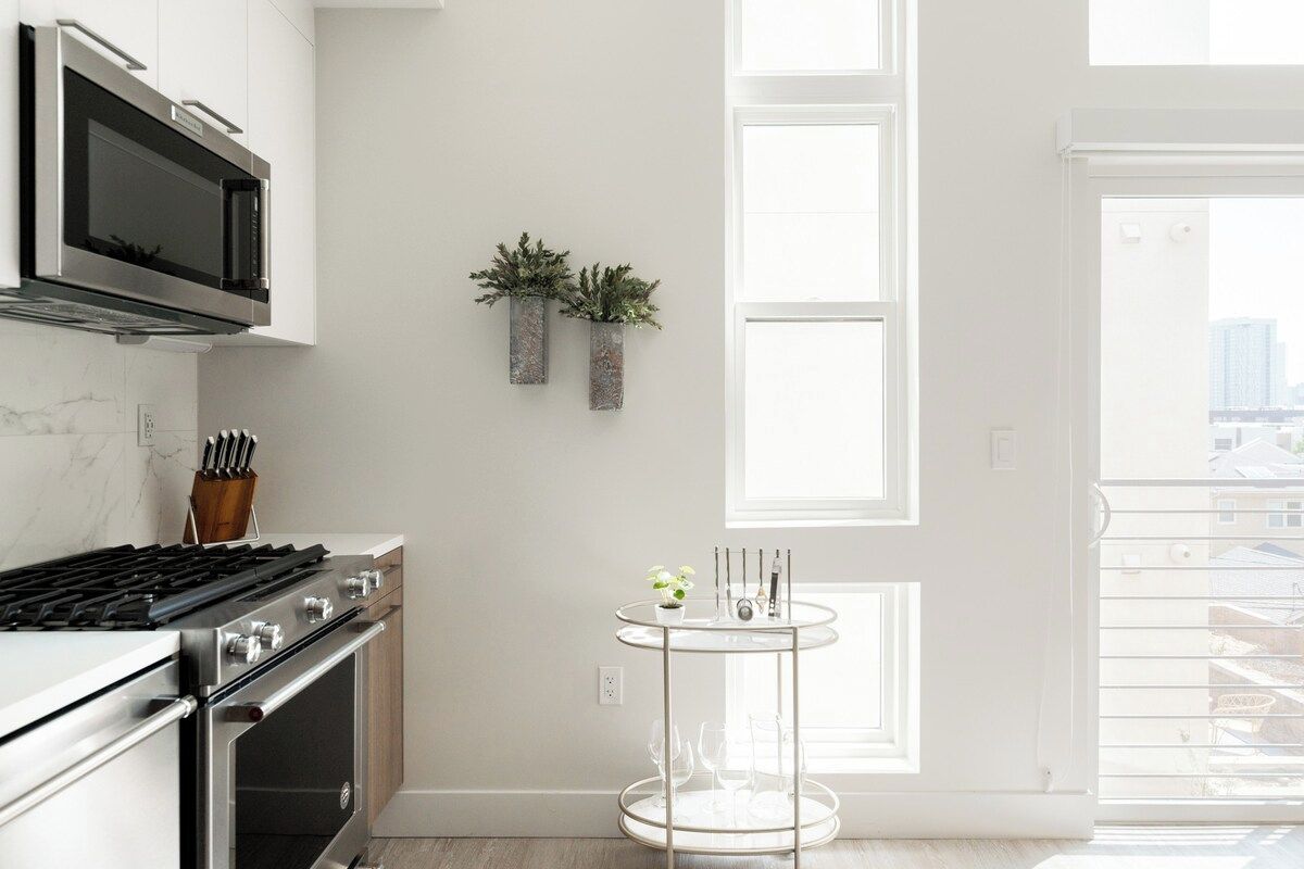 Une cuisine moderne équipée d’appareils électroménagers en acier inoxydable, une table ronde en verre et une fenêtre donnant sur la ville.