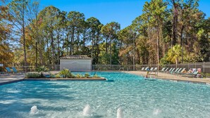 A swimming pool with clear water, surrounded by trees and a fenced area with lounge chairs.