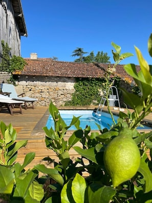 Una terraza de madera con piscina, un muro de piedra y vistas a un edificio tradicional.
