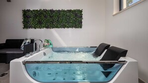 A modern bathroom with a freestanding bathtub, a green leafy wall decoration, and a window providing natural light.