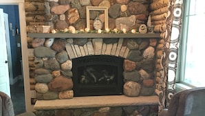 A stone fireplace with a clock and decorative items, flanked by two armchairs and a small table with candles. - Stonehaven Cottages - "The Birchview Suite Duplex - Lower Level" (Rice Lake)