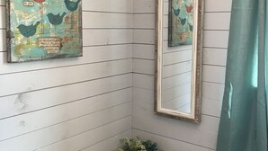A bathroom with white wooden walls, a white vase with flowers, a mirror, and a teal shower curtain. - Stonehaven Cottages - "The Birchview Suite Duplex - Lower Level" (Rice Lake)